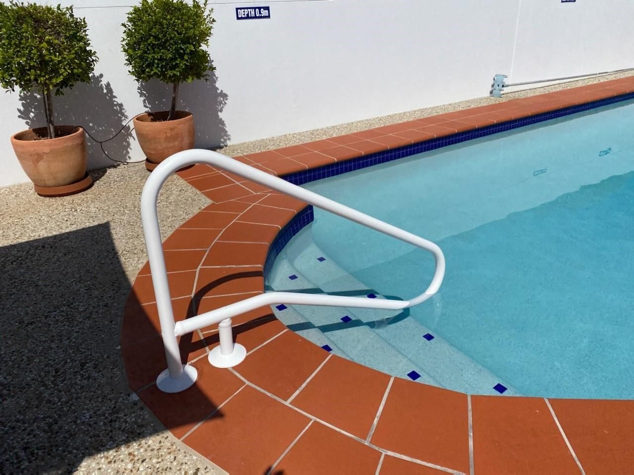 Outdoor swimming pool with terracotta tile edging and white safety handrail