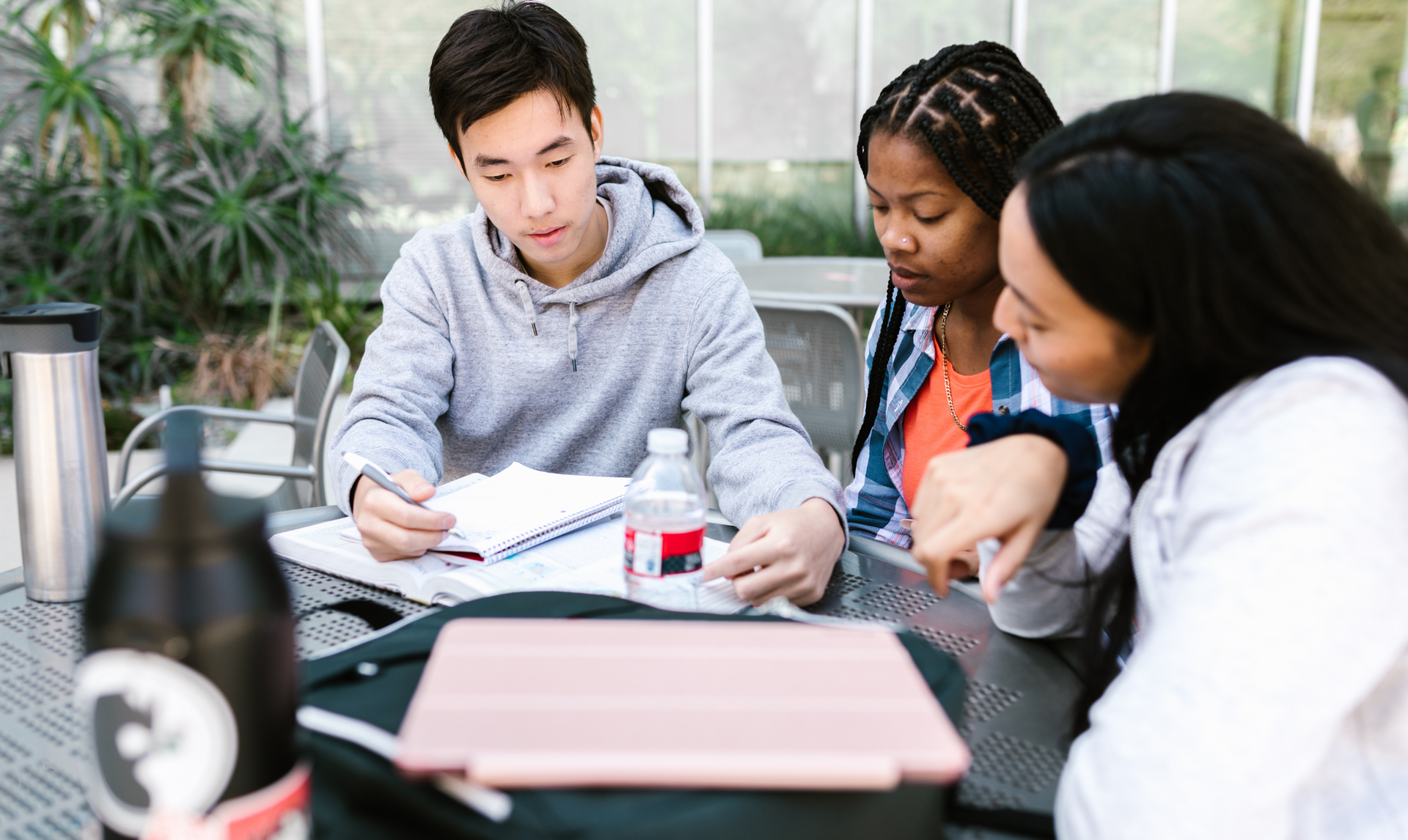 A group of young people are sitting at a table looking at a tablet.