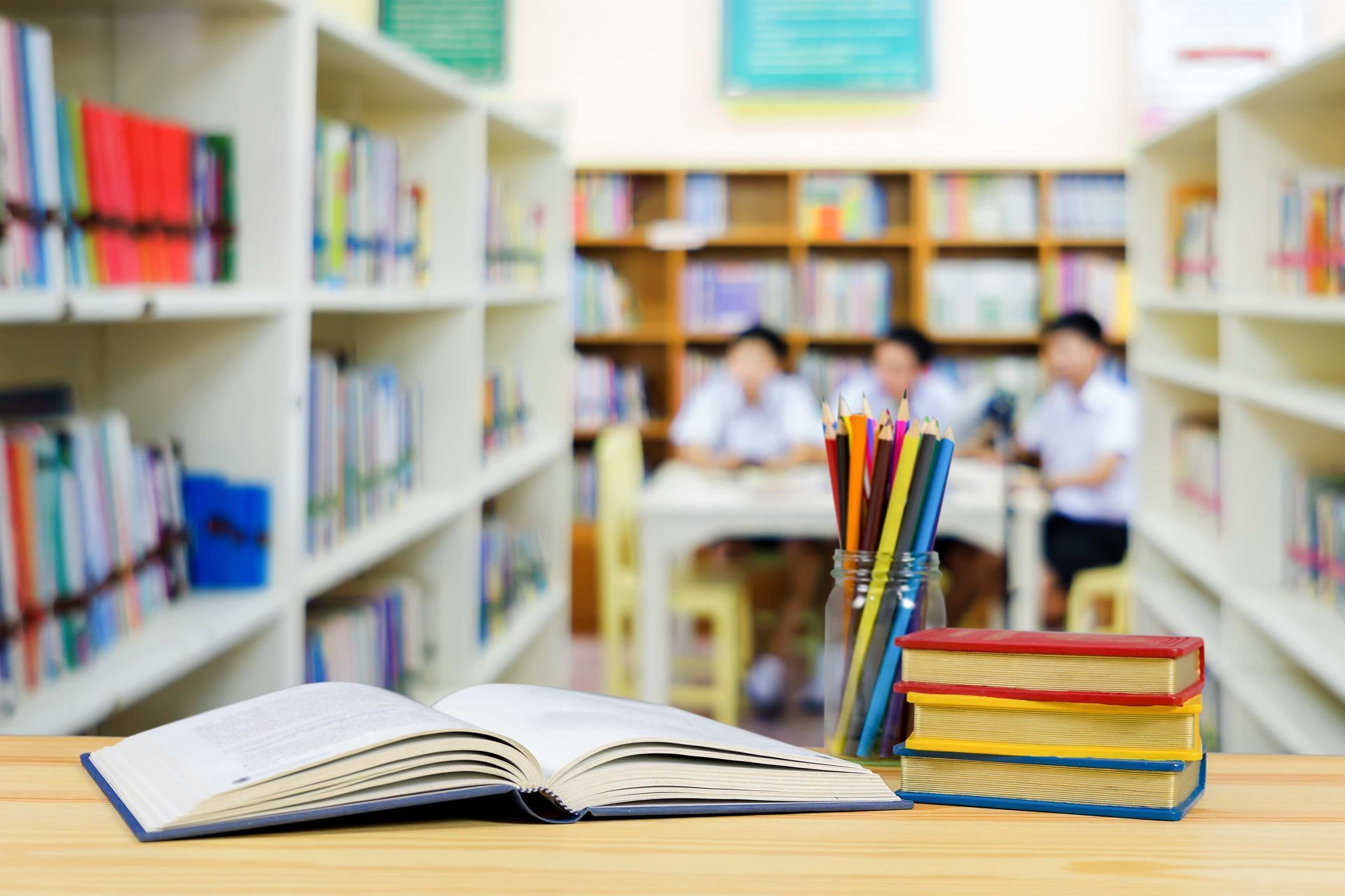 A stack of books and pencils on a wooden table in a library.
