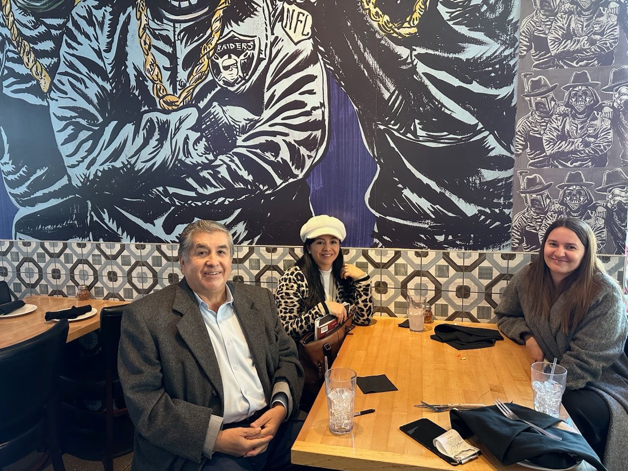A group of people are sitting at a table in front of a mural.
