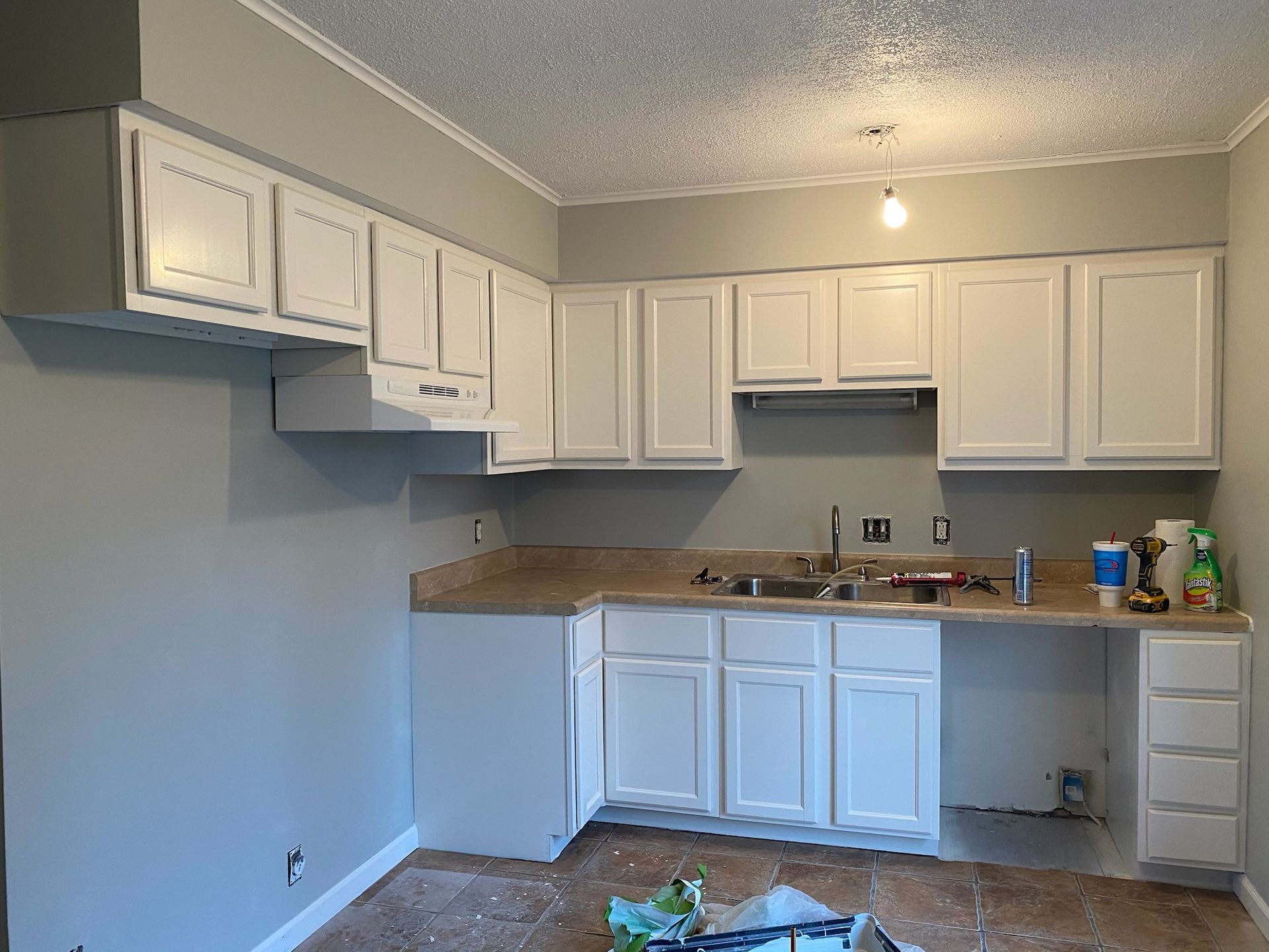 Kitchen with white cabinets, light countertops, and sink. Wall is light gray, ceiling is textured.