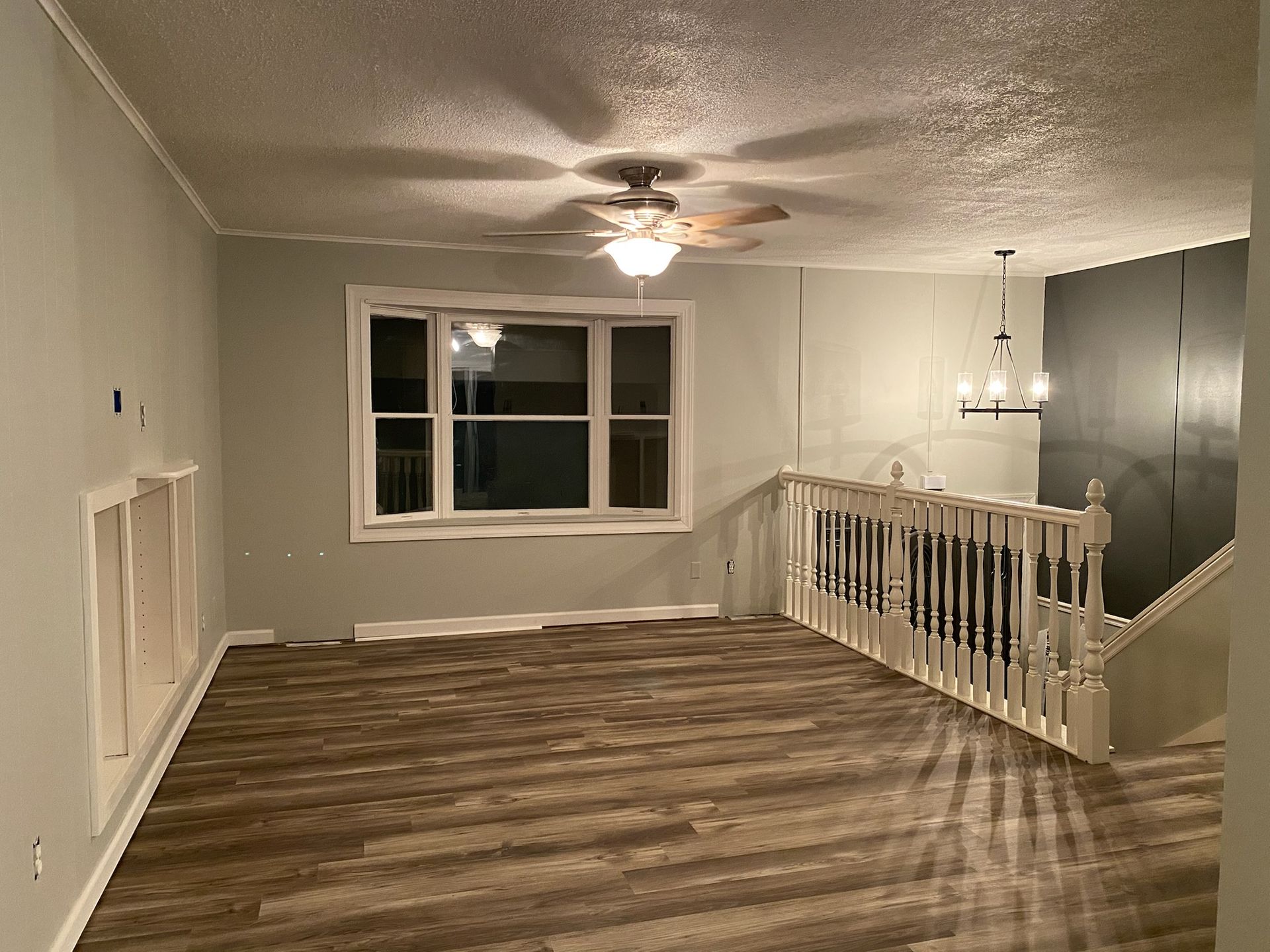 Empty room with gray walls, wood-look flooring, ceiling fan, and staircase.