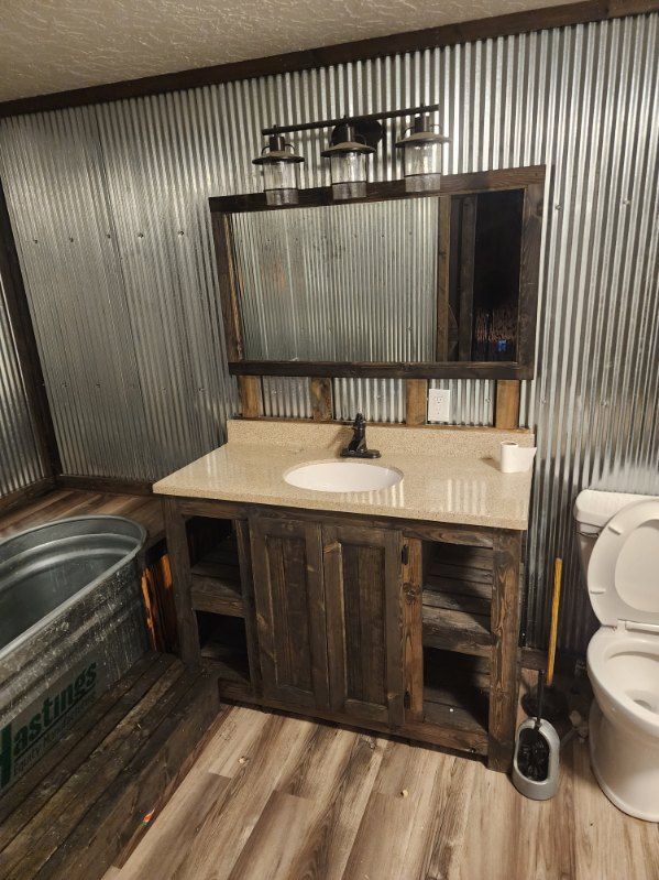 Rustic bathroom with corrugated metal walls, wood vanity, mirror, and a galvanized tub.