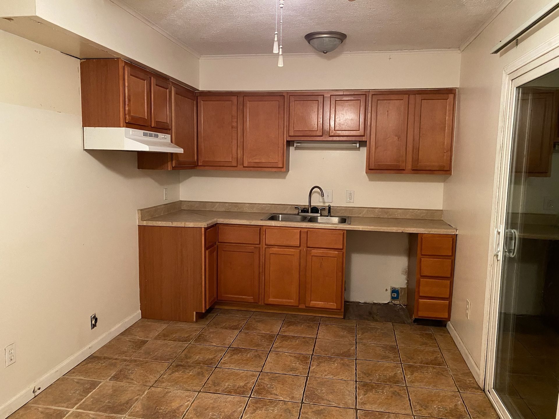 Kitchen with brown cabinets, countertop, and tiled floor; a sliding door is to the right.
