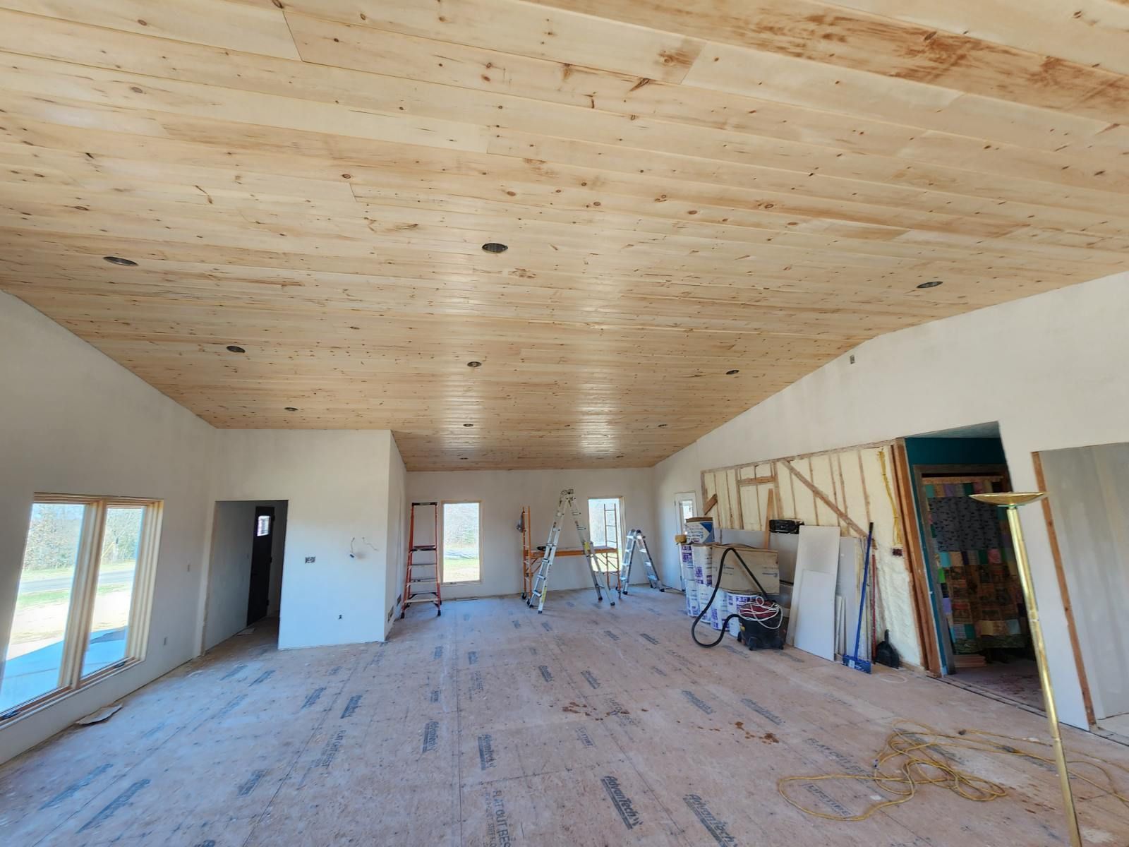 Interior under construction with a wood plank ceiling and unfinished walls and floors.