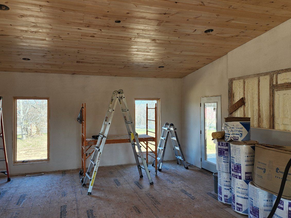 Interior of a room under construction with wood ceiling, ladders, and insulation.
