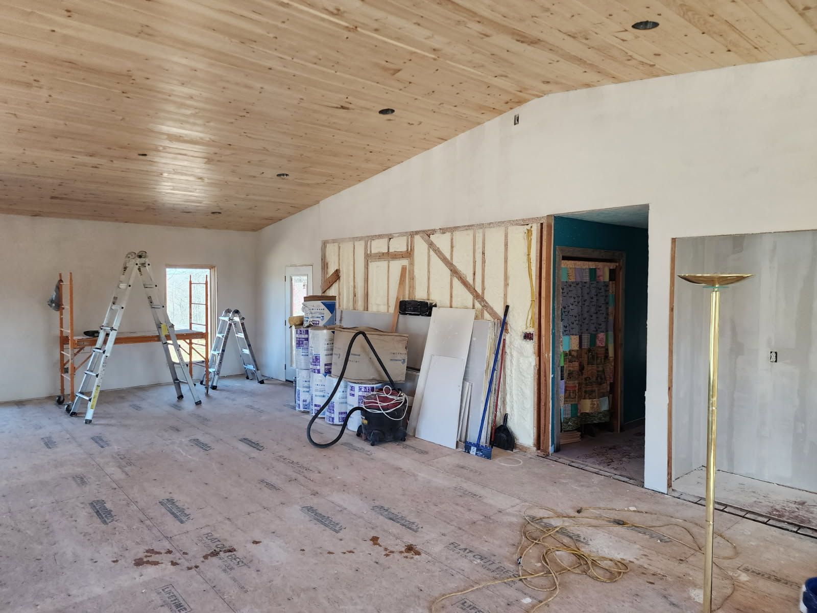 Interior room under construction, with wood ceiling, drywall, and tools scattered about.
