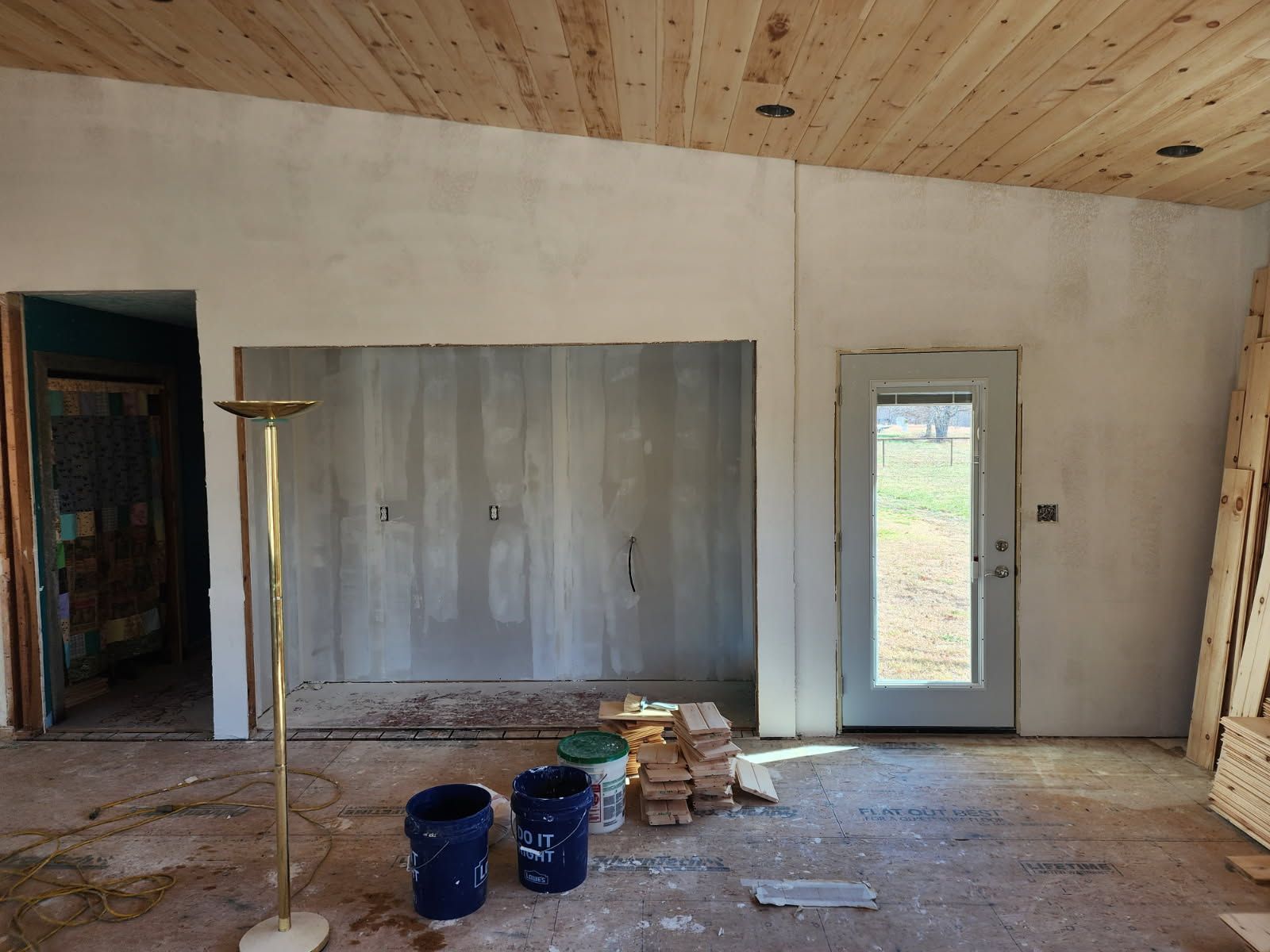Interior room under construction, with textured gray wall, wooden ceiling, door to outside.