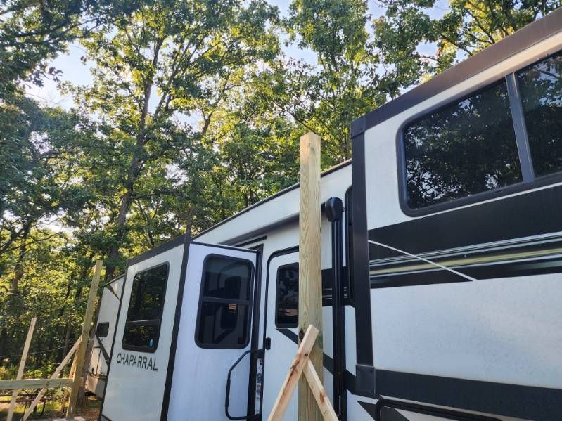 RV with wooden support posts in front of the door; trees in the background.