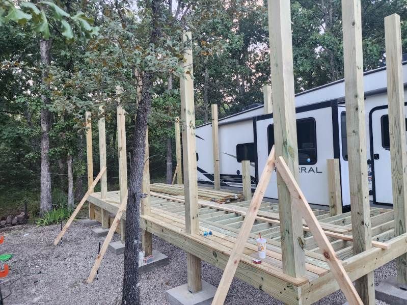 Wooden deck under construction next to a parked camper. Gray concrete blocks support the deck structure.