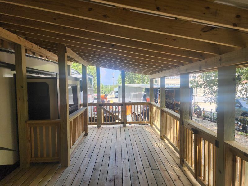 Wooden porch with railing and roof, newly constructed. Bright, sunny setting.