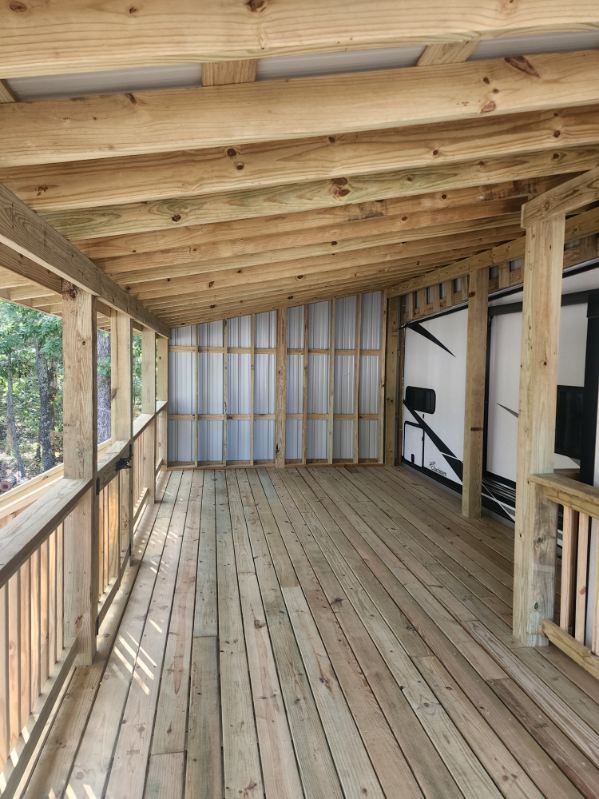 Wooden porch with railing and roof, extending from a structure. Natural wood color.