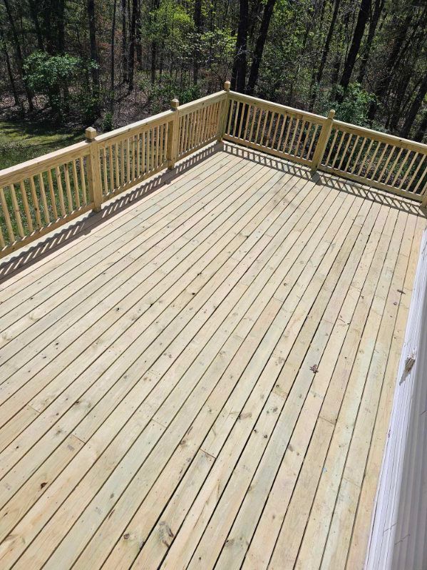 Wooden deck with railing overlooking a wooded area. The deck is constructed of light-colored wood.