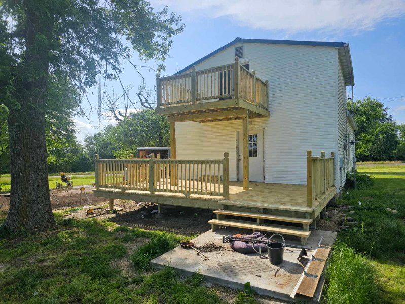 Two-story white house with wooden decks. The first deck is ground-level, the second is a balcony. Sunny day.