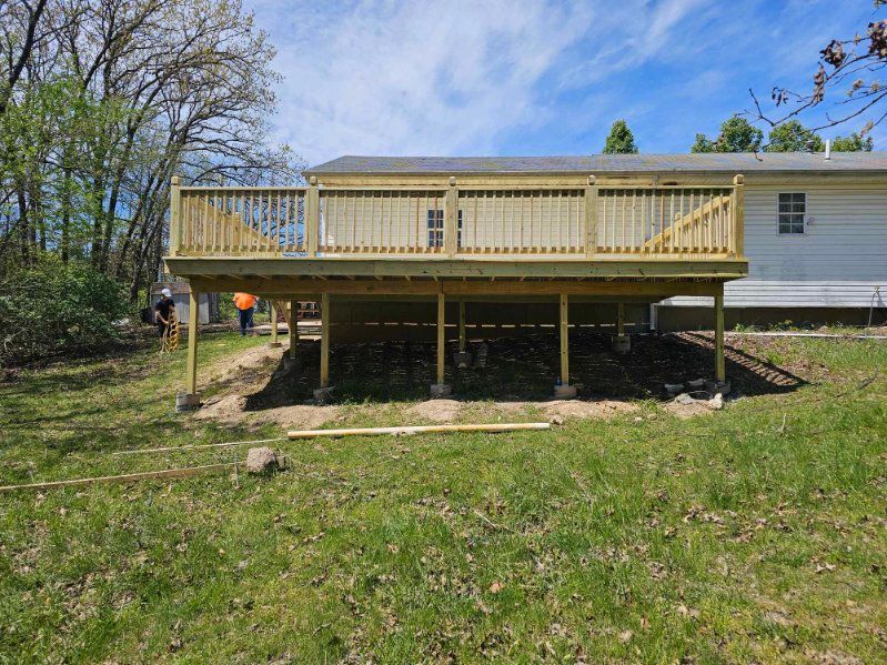 Wooden deck being built, set in a grassy yard, supported by wooden posts. Sunny day.