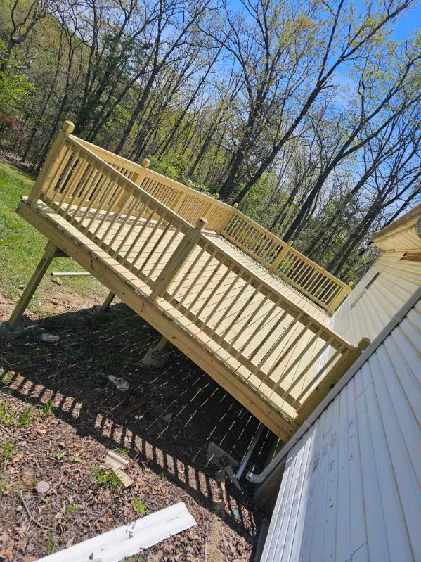 New wooden deck attached to a house with railing, set in a yard with trees.