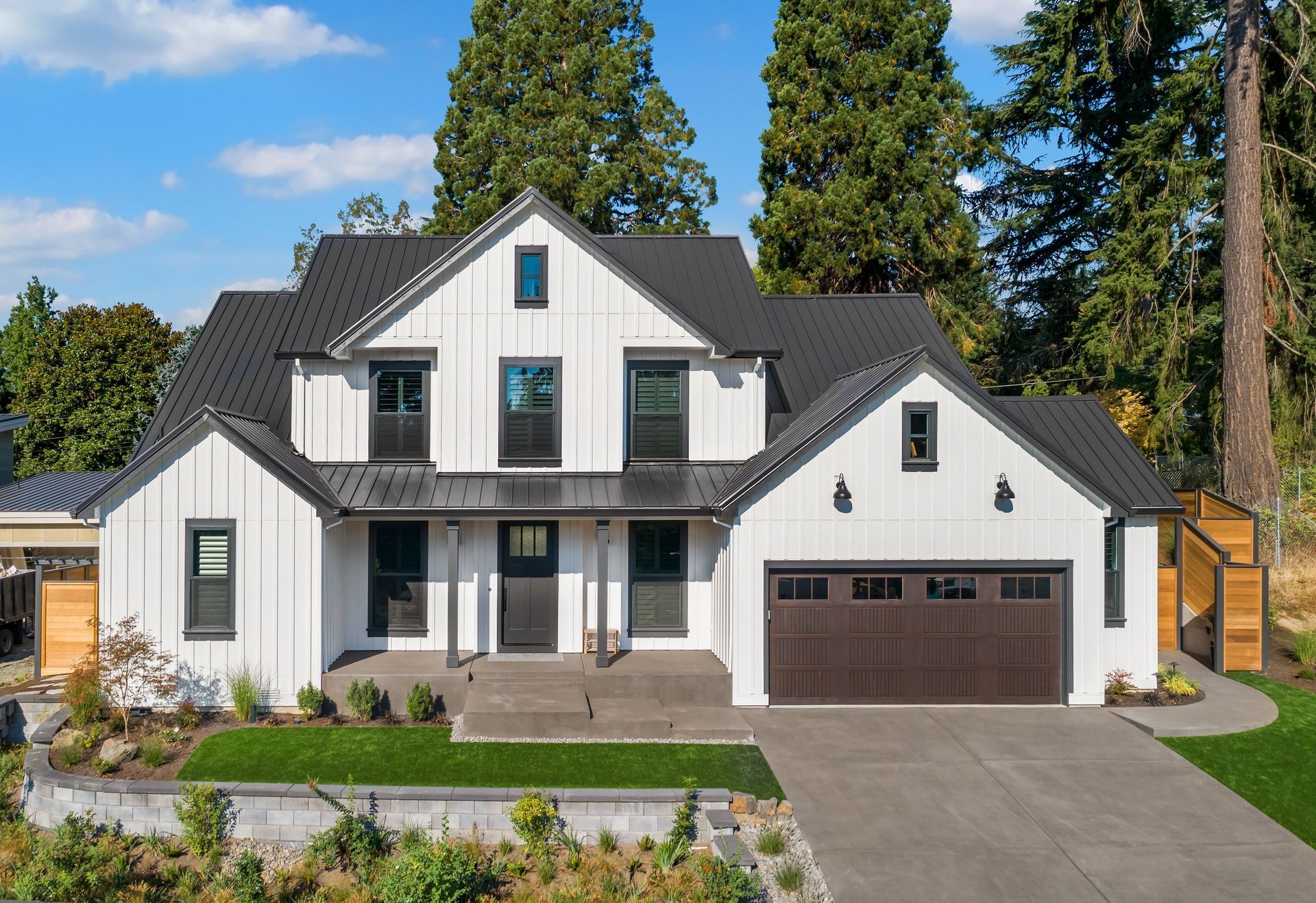 White farmhouse with black trim, dark brown garage door, and lush green lawn.