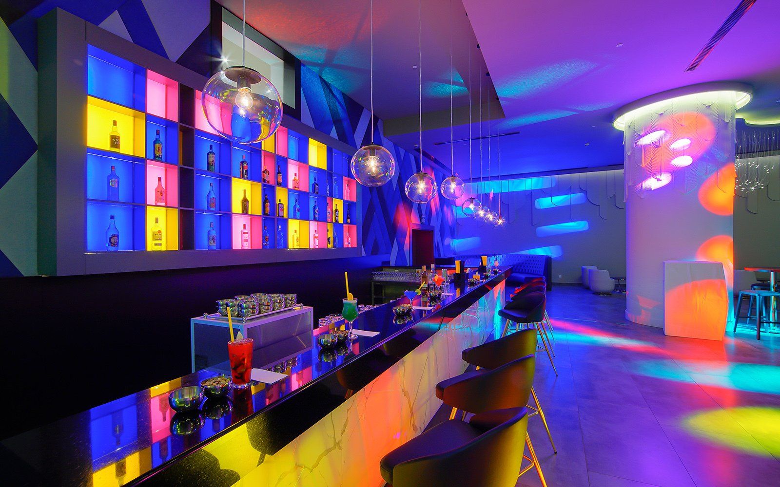 Un bar dans un club avec des lumières colorées sur les murs et le plafond.