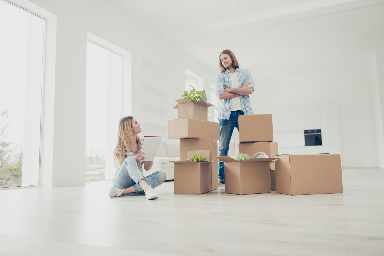 A man and a woman are sitting on the floor next to a pile of cardboard boxes.