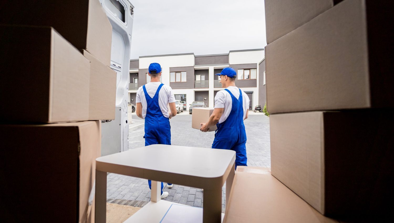 Two men are carrying boxes and a table into a house.