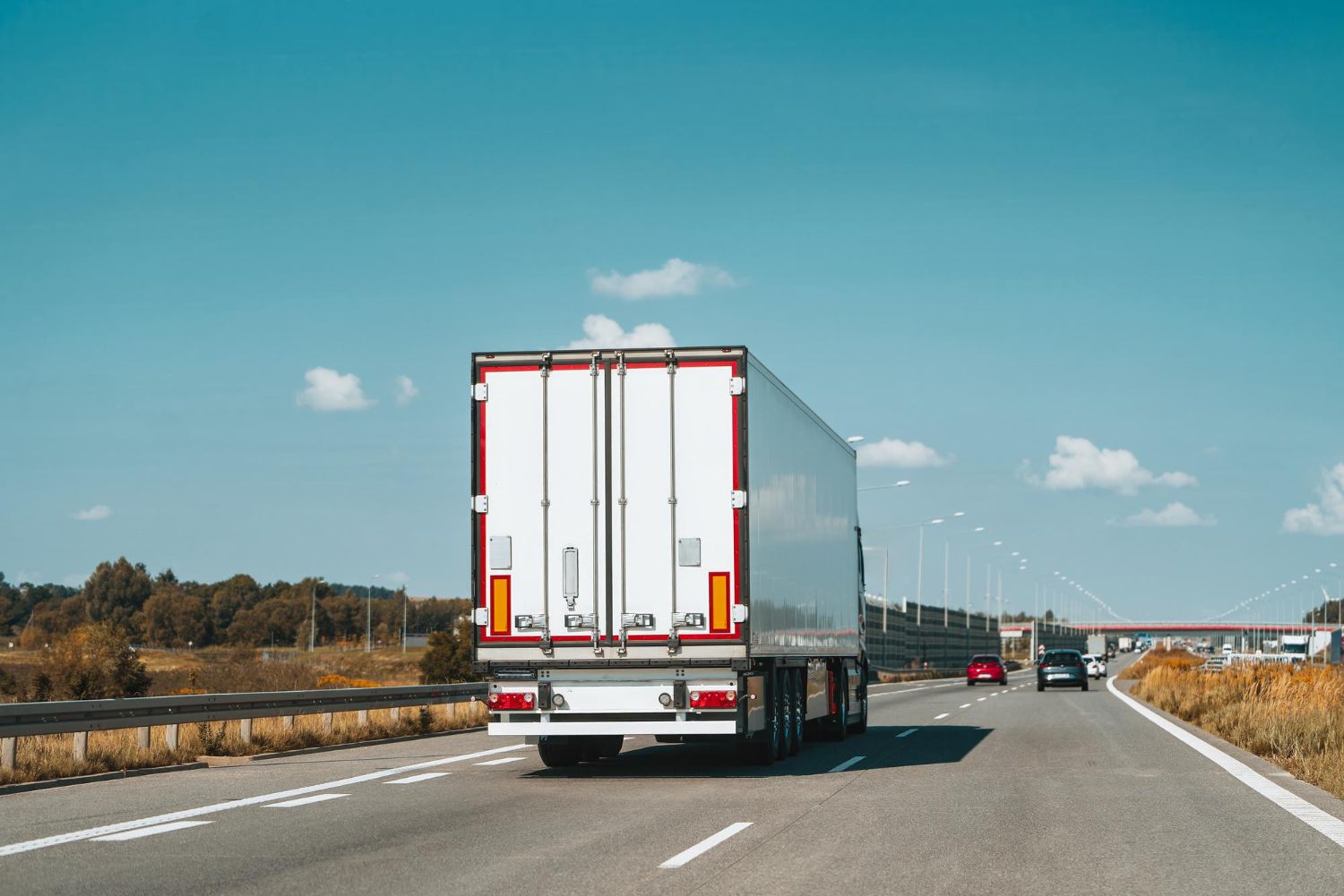 White semi-truck driving on a highway with blue sky and scattered clouds.