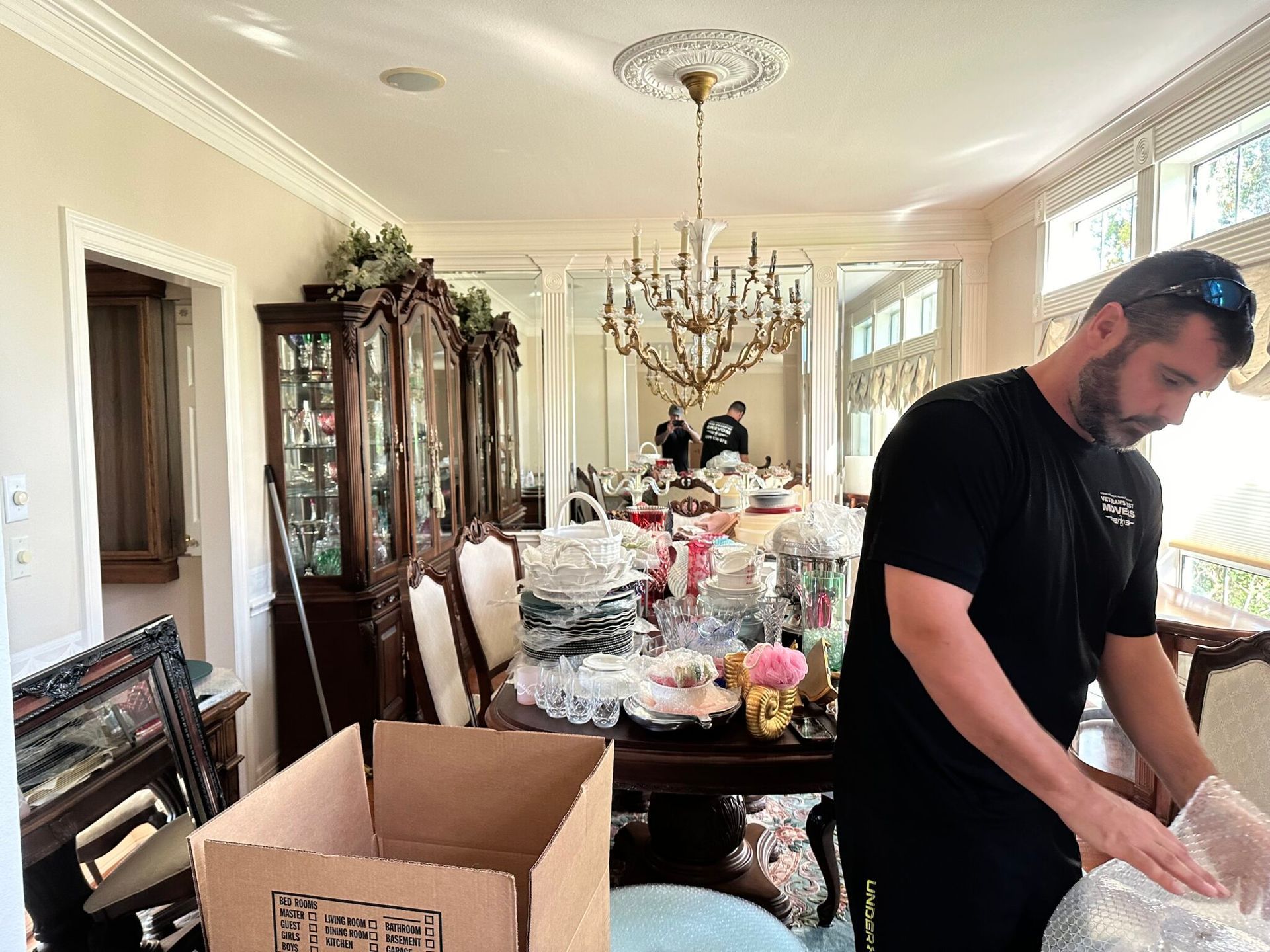 A man is packing a cardboard box in a dining room.