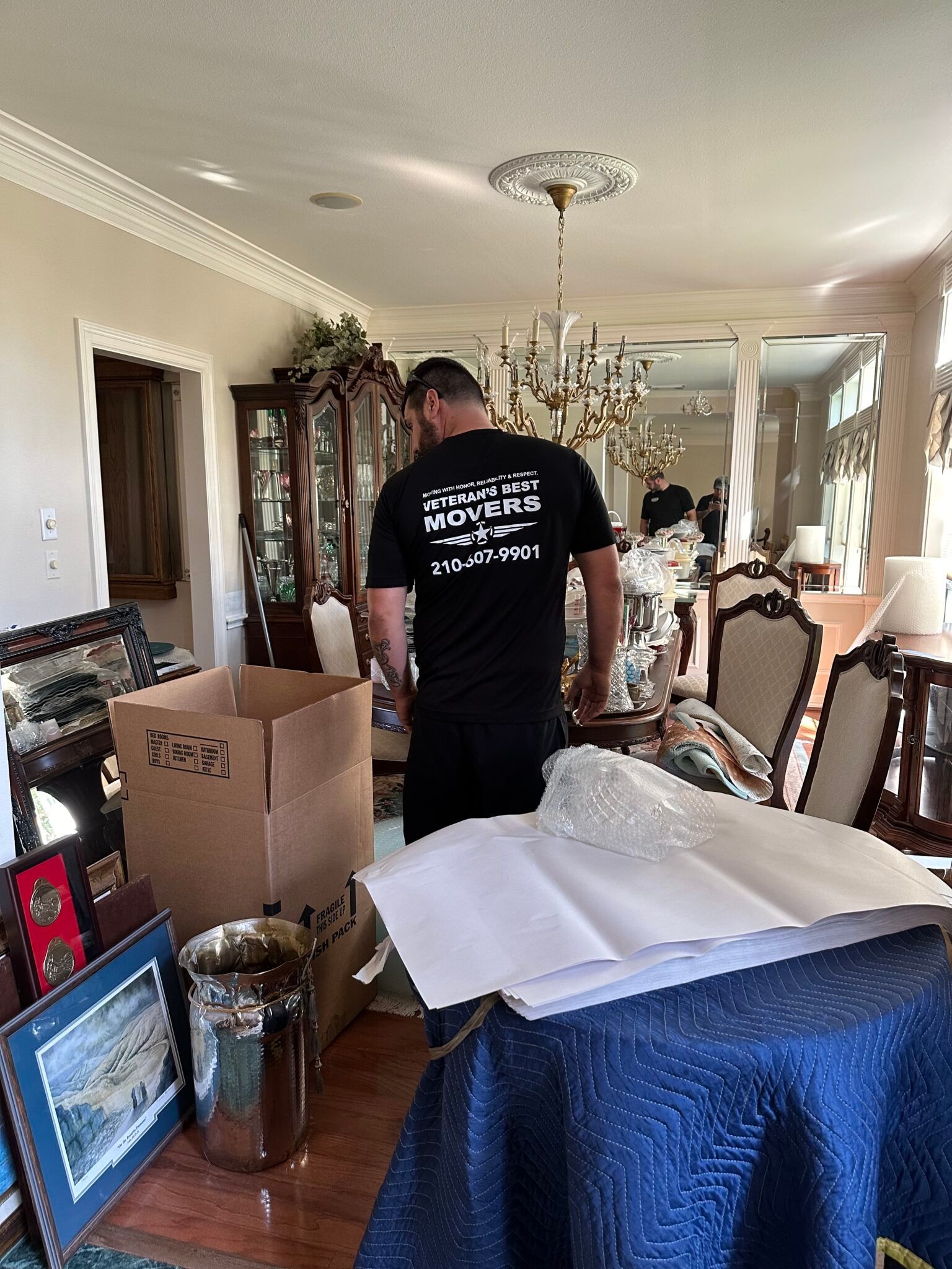 A man is standing in a living room filled with boxes and paintings.