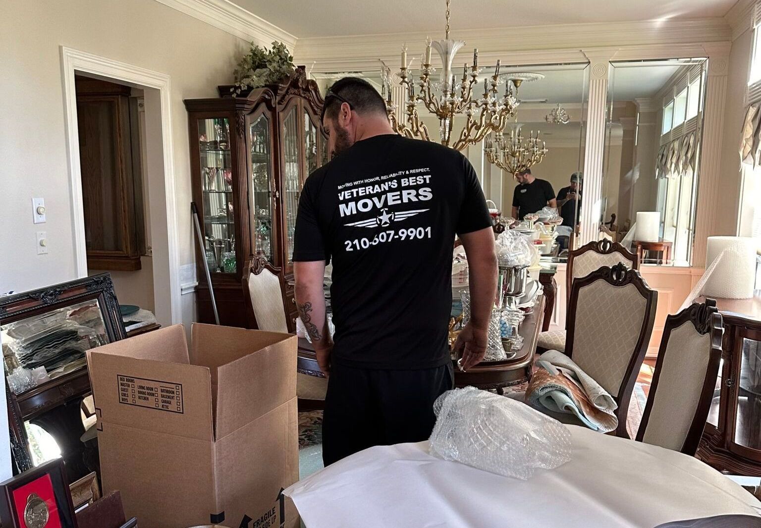 A man is standing in a dining room holding a cardboard box.