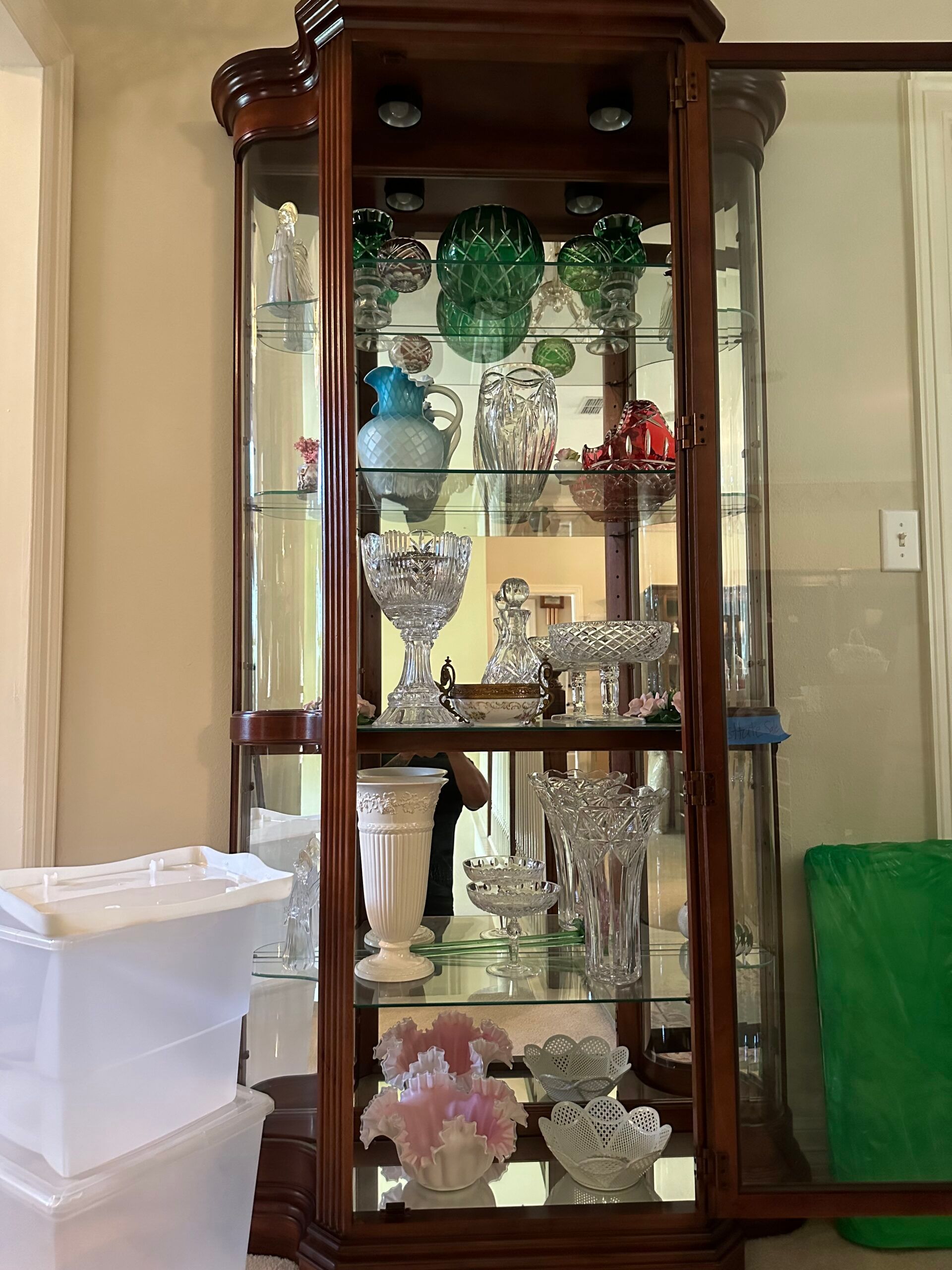 A glass curio cabinet filled with lots of glassware and vases.