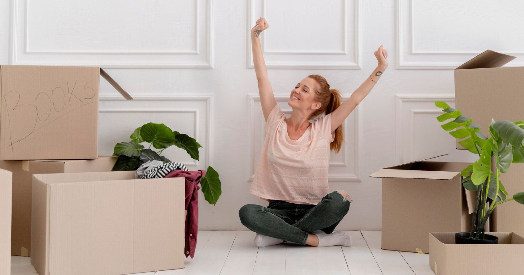 A woman is sitting on the floor in a room surrounded by cardboard boxes.