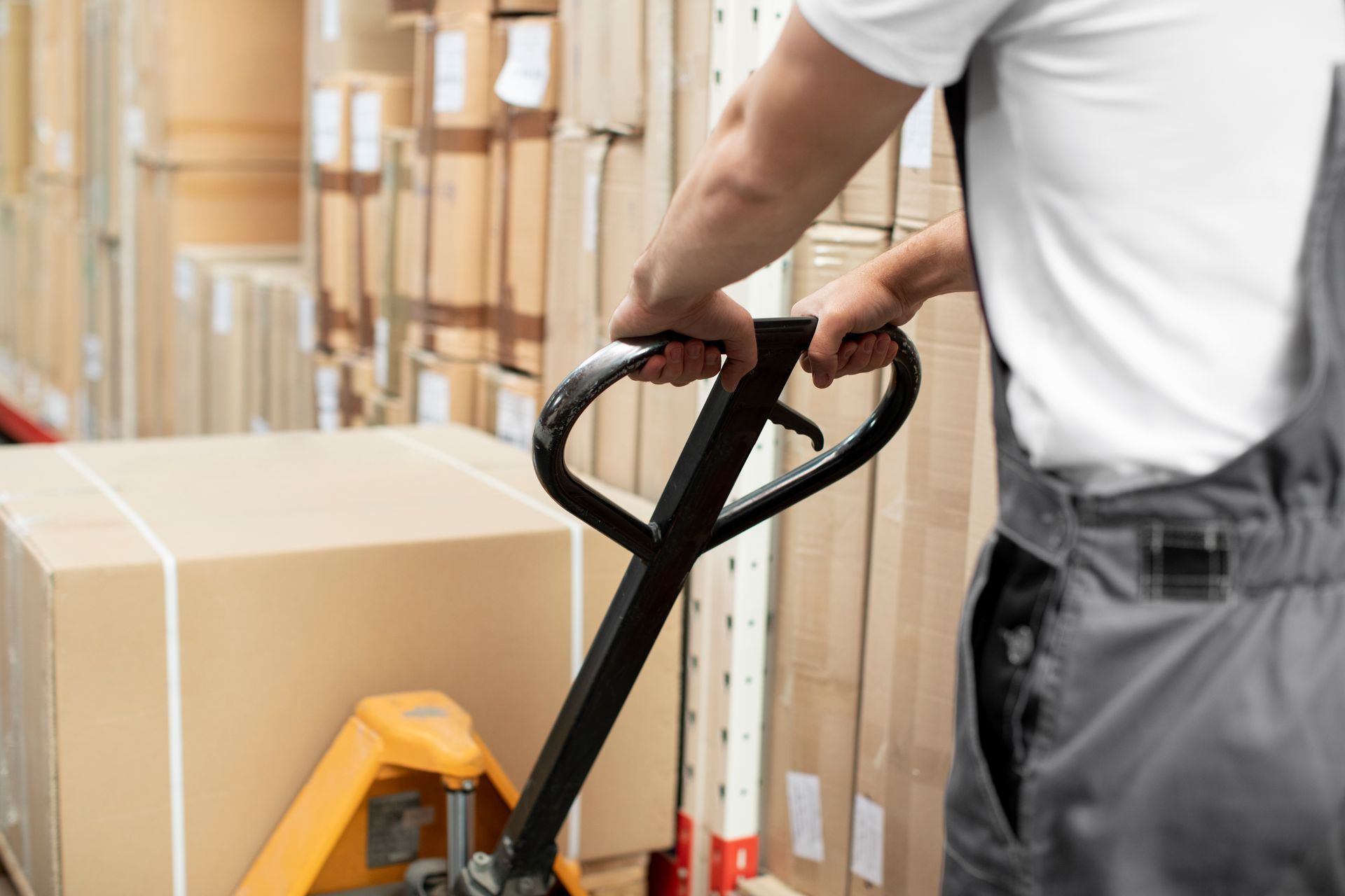 A man is pushing a pallet truck in a warehouse.