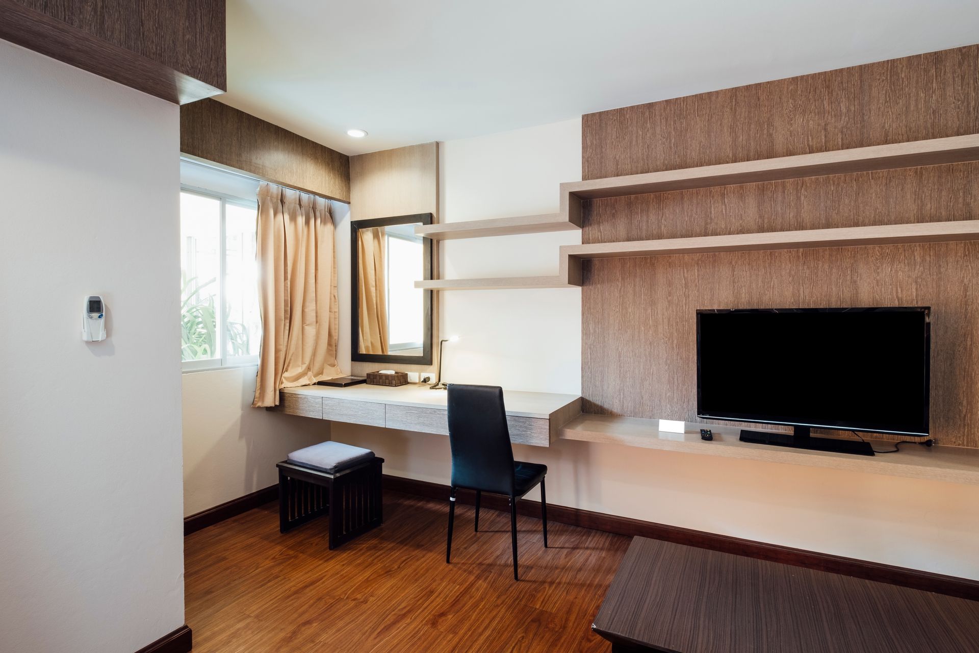 A living room with a desk , chair , television and mirror.