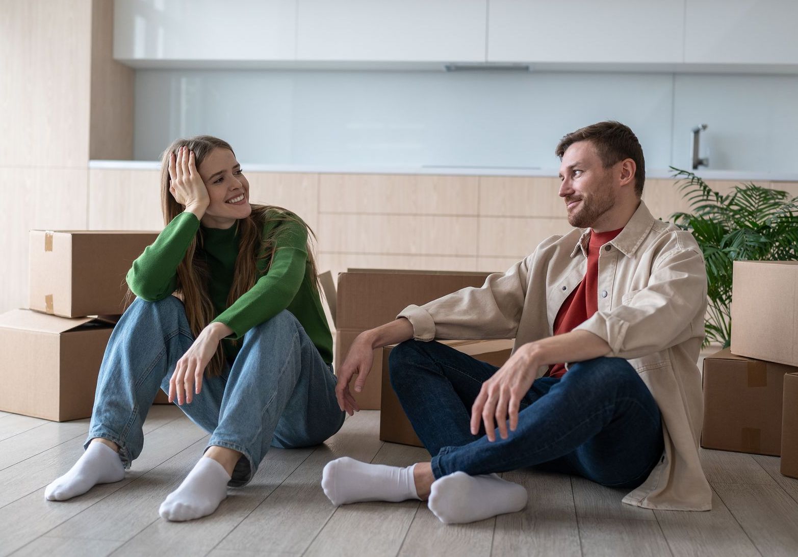 A man and a woman are sitting on the floor in their new home surrounded by cardboard boxes.