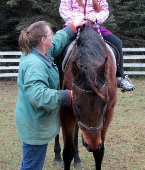 Woman in a green coat helping a horseback rider with the reins