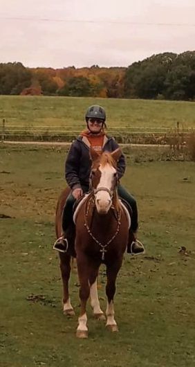 A woman is riding a brown horse in a field.