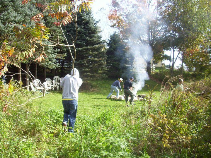 a group of people are picking up sticks and gathered around a fire in a backyard
