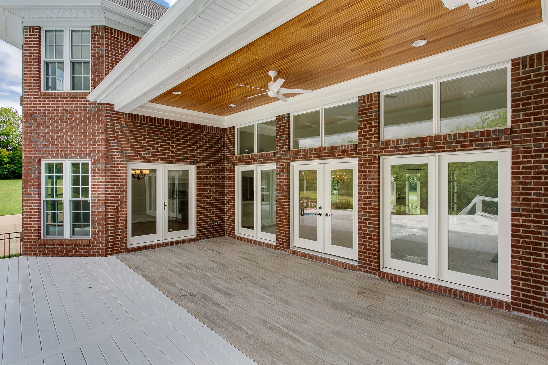 Brick patio with white-trimmed French doors and a covered wood-paneled porch outside a house