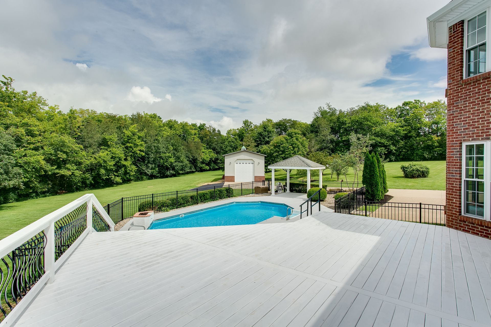 Spacious white deck overlooking a blue pool, gazebo, and green backyard beside a brick house