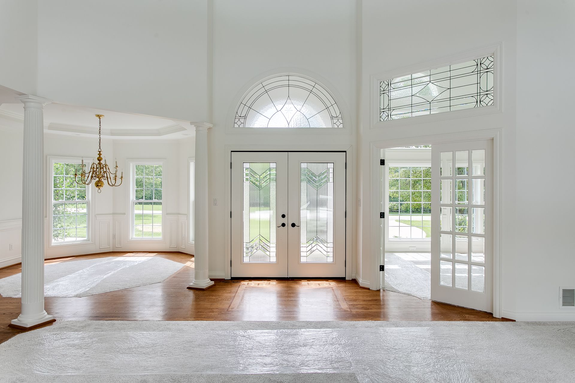 Bright, empty living room with white walls, hardwood floors, and large glass doors and windows.