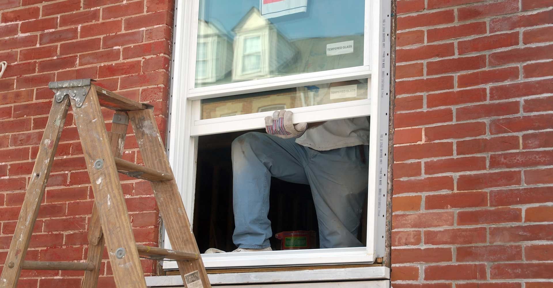 Person working in an open window beside a brick wall, with a wooden ladder leaning nearby.