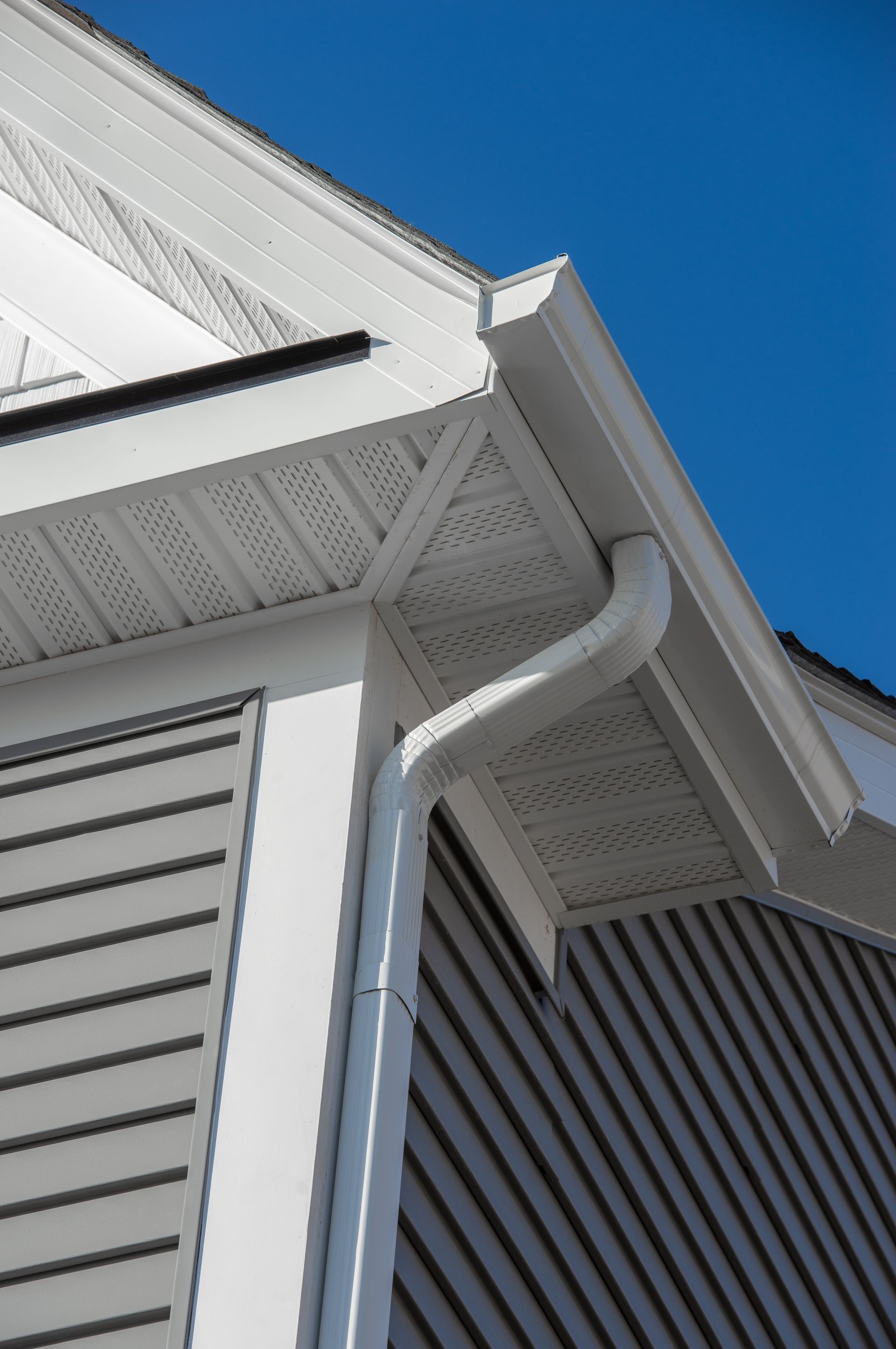 White house eaves and downspout against a clear blue sky