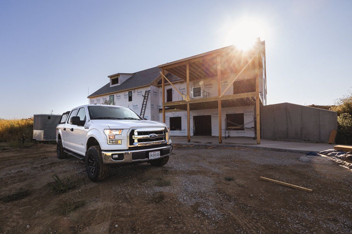 A white truck is parked in front of a house under construction.