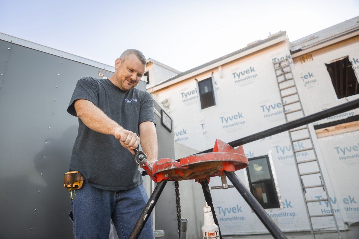A man is working on a pipe in front of a building under construction.