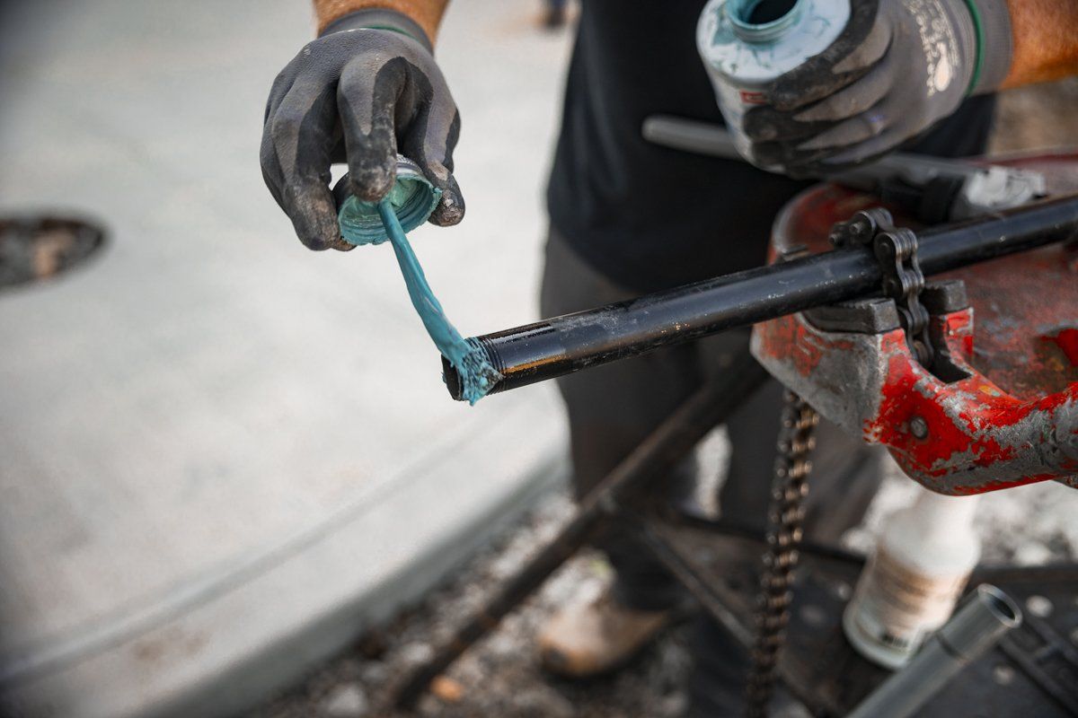 A man is applying grease to a pipe with a wrench.