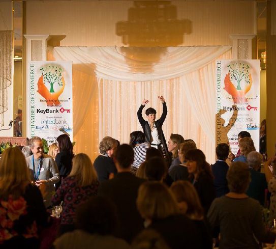 A woman stands on a stage with her arms in the air in front of a crowd