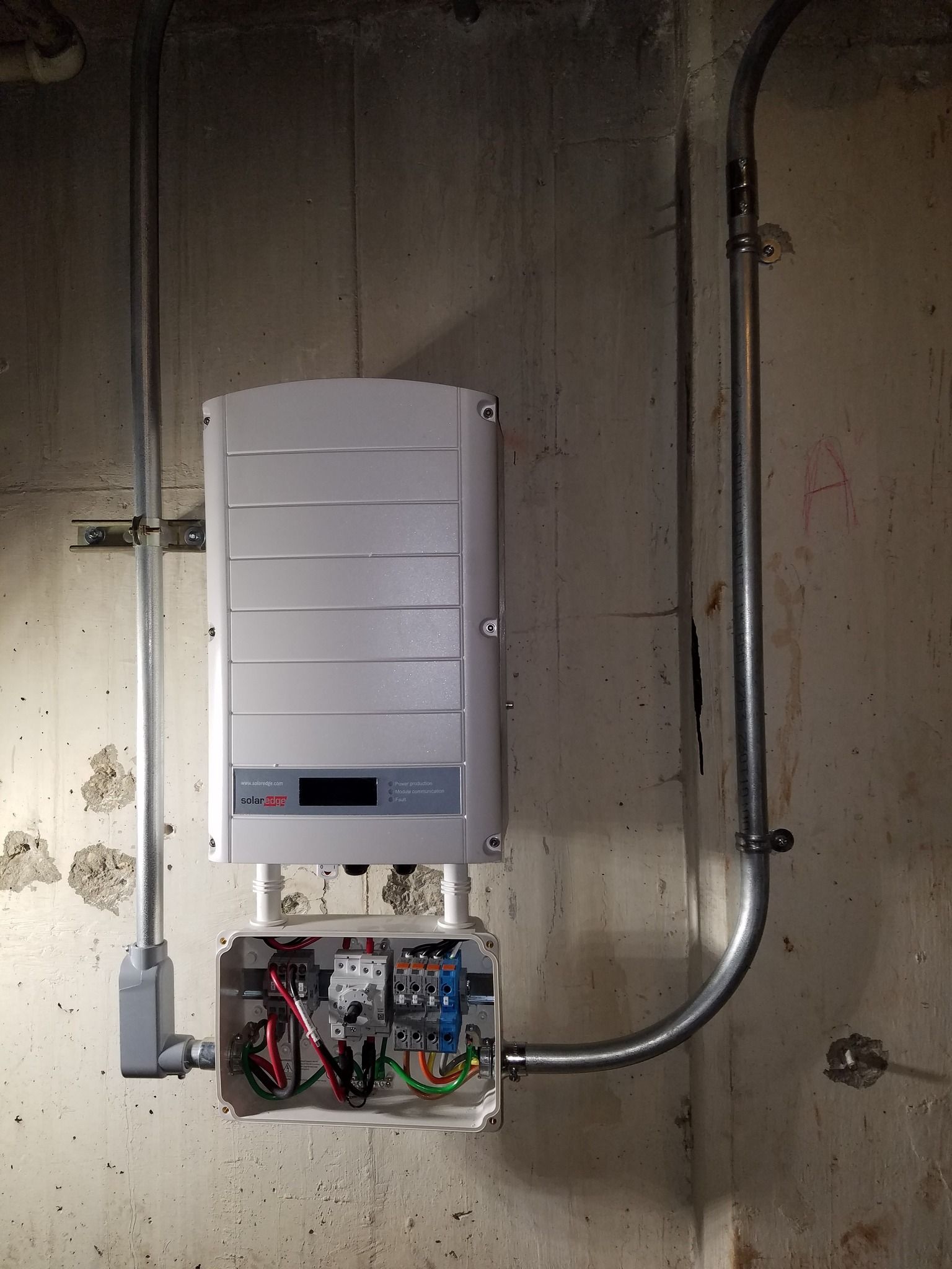 Solar inverter and electrical box mounted on a concrete wall with conduit.