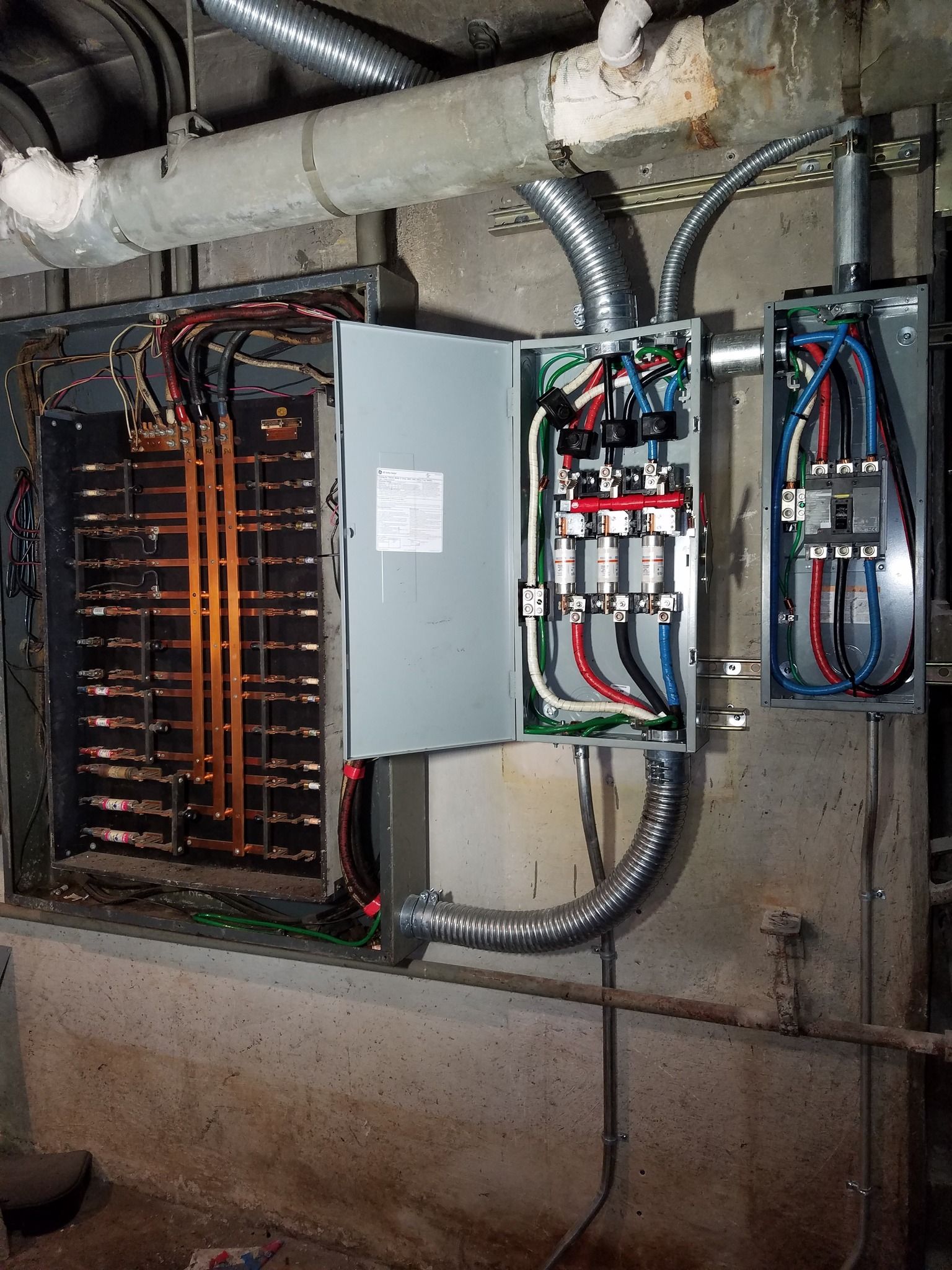 Electrical panel with wiring and conduit in a concrete basement setting.