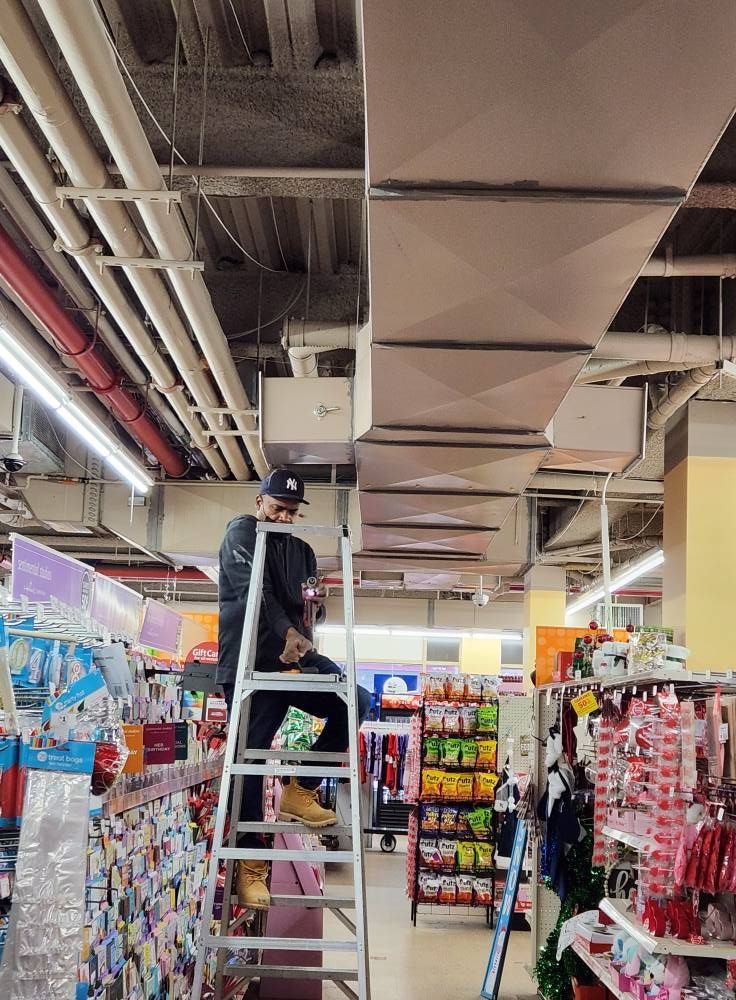 A person on a ladder working on ceiling fixtures in a store.