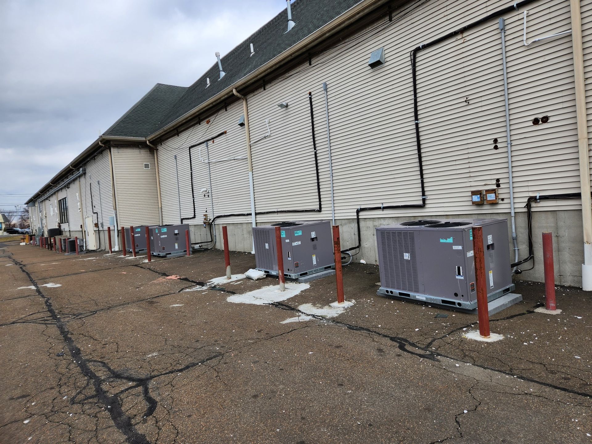 Exterior view of building with HVAC units along its side. Brown/gray units sit on concrete with support posts.