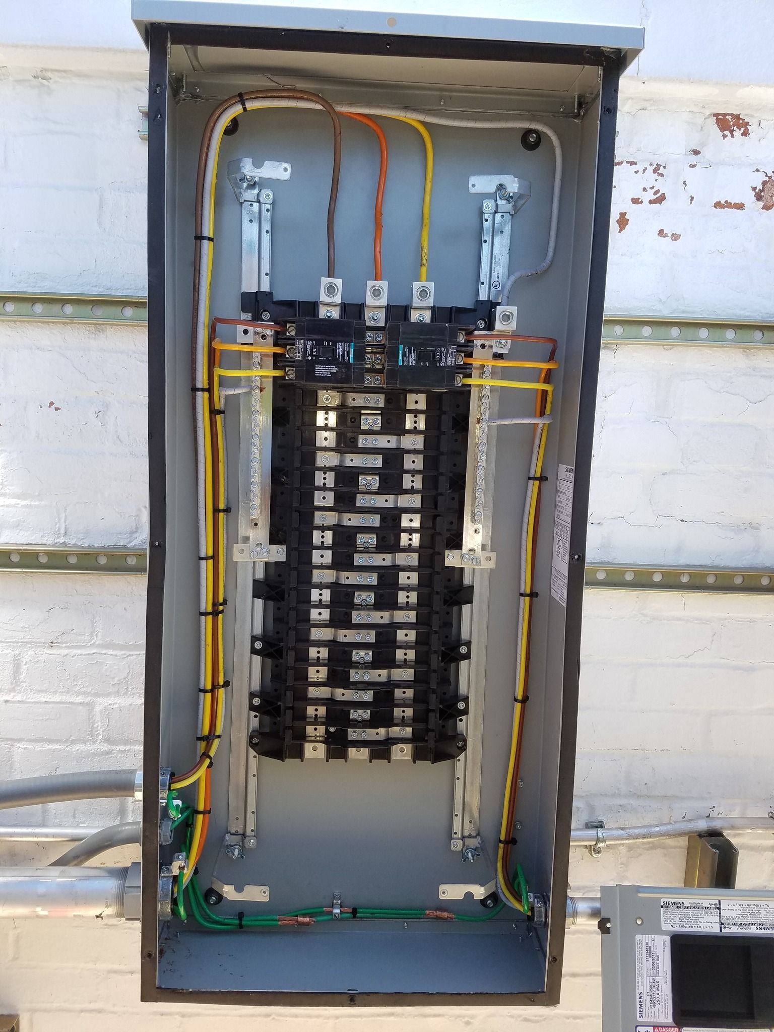 Open electrical panel with wires and circuit breakers. Yellow, orange, and green wires against a gray background.